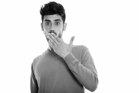 Studio shot of young Persian man looking surprised while covering mouthの写真素材