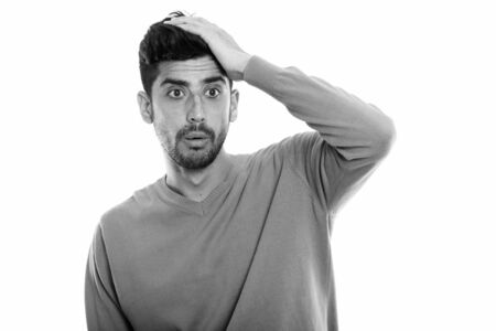 Studio shot of young Persian man looking shocked with hand on head