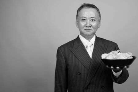 Portrait of mature Asian businessman against gray backgroundの写真素材