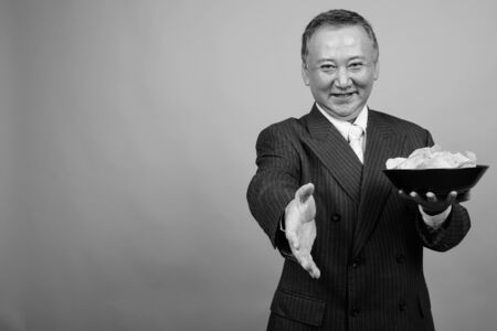 Portrait of mature Asian businessman against gray backgroundの写真素材