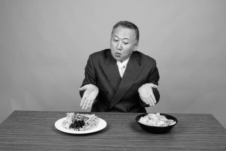 Mature Asian businessman sitting with wooden table against gray backgroundの写真素材
