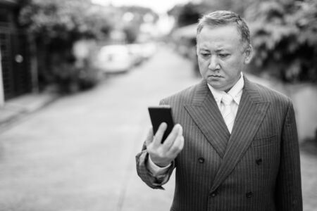 Mature Asian businessman using mobile phone in the streets outdoorsの写真素材