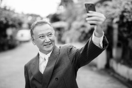 Mature Asian businessman using mobile phone in the streets outdoorsの写真素材