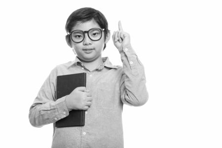 Studio shot of cute Japanese boy holding book and pointing finger upの写真素材