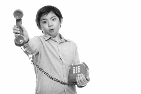 Studio shot of cute Japanese boy giving old telephone looking shocked