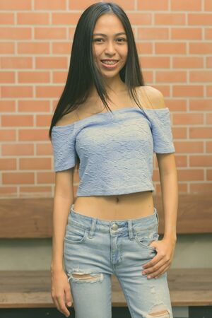 Young beautiful Asian teenage girl against brick wall