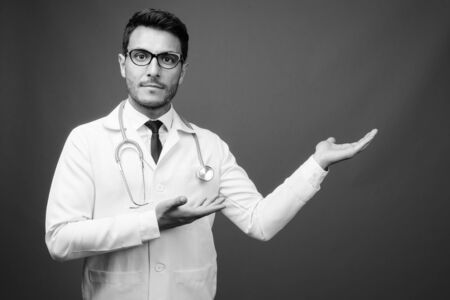 Young handsome Hispanic man doctor against grayの写真素材