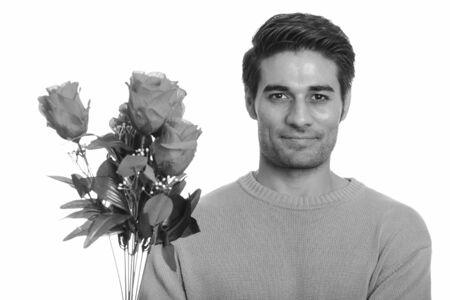 Young handsome Persian man holding red roses ready for Valentines dayの写真素材