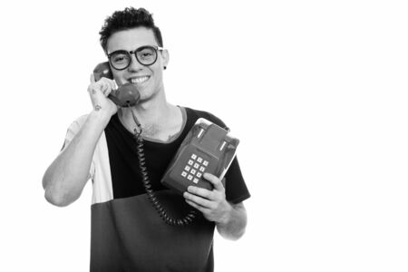 Studio shot of happy young man smiling while talking on old telephoneの写真素材