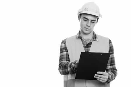 Studio shot of young man construction worker reading on clipboardの写真素材