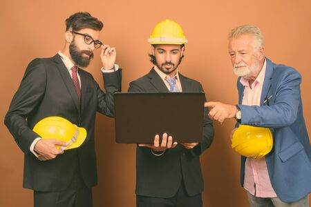 Three multi ethnic bearded businessmen together against brown backgroundの写真素材