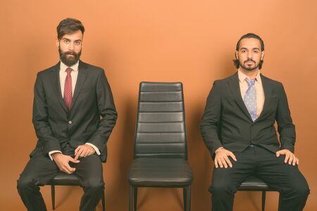 Two multi ethnic bearded businessmen together against brown backgroundの写真素材