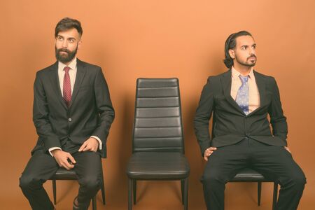 Two multi ethnic bearded businessmen together against brown backgroundの写真素材