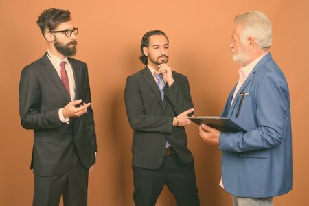 Three multi ethnic bearded businessmen together against brown background