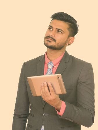 Young handsome bearded Indian businessman using digital tablet and thinkingの写真素材