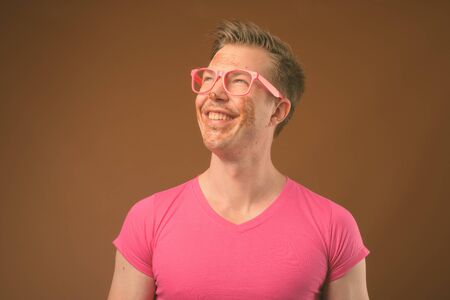 Young handsome man wearing pink shirt and eyeglasses against brown background
