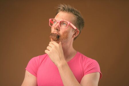 Young handsome man wearing pink shirt and eyeglasses against brown background
