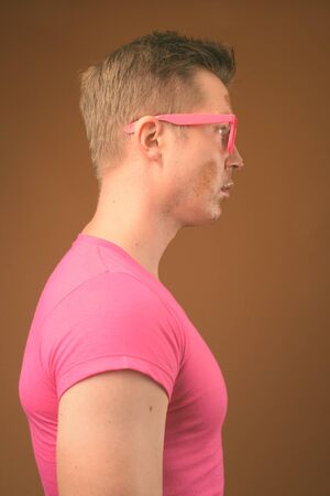 Young handsome man wearing pink shirt and eyeglasses against brown backgroundの写真素材
