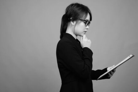 Young beautiful Asian businesswoman against gray backgroundの写真素材