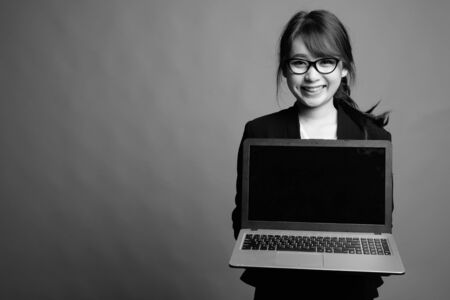 Young beautiful Asian businesswoman against gray background