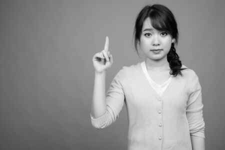 Young beautiful Asian woman wearing cardigan against gray backgroundの写真素材