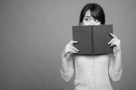 Young beautiful Asian woman holding book against gray backgroundの写真素材