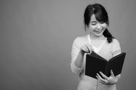 Young beautiful Asian woman holding book against gray backgroundの写真素材