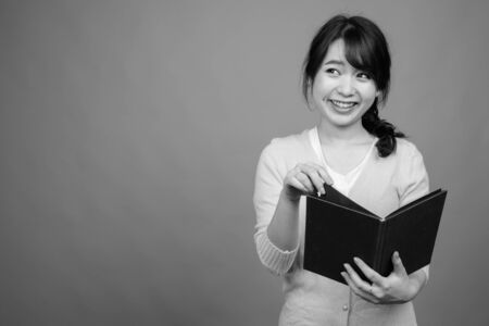Young beautiful Asian woman holding book against gray backgroundの写真素材