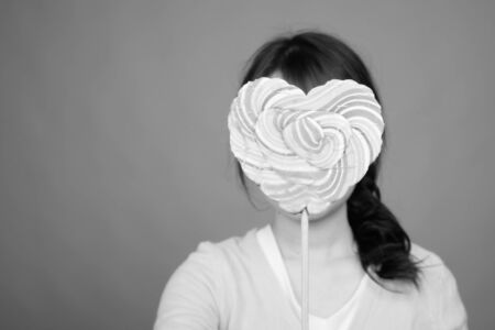 Young beautiful Asian woman holding heart shaped lollipop
