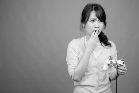 Young beautiful Asian woman playing games against gray backgroundの写真素材