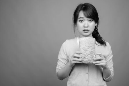 Young beautiful Asian woman holding bread against gray backgroundの写真素材