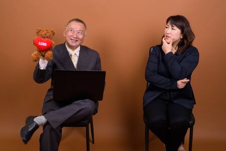 Mature Asian businesswoman with mature Asian businessman using laptop