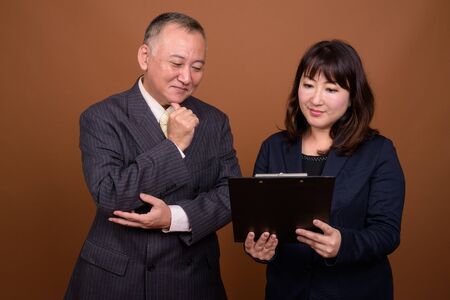 Mature Asian businessman and mature Asian businesswoman reading on clipboard togetherの写真素材