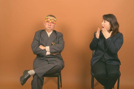 Mature Asian businessman and mature Asian businesswoman together against brown backgroundの写真素材