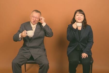 Mature Asian businessman and mature Asian businesswoman together against brown background