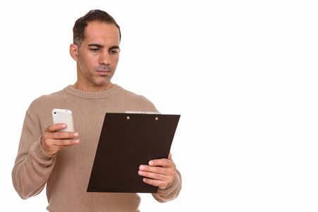 Mature handsome Persian man using phone while reading on clipboard