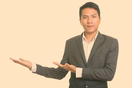 Studio shot of young Asian businessman showing something