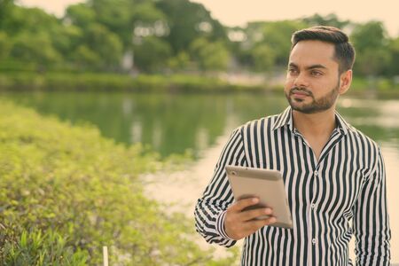 Young bearded Indian businessman relaxing at the park