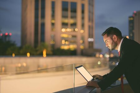 Young bearded Indian businessman against view of the city at night