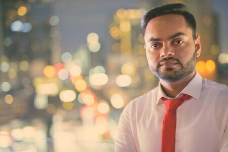 Young bearded Indian businessman against view of the city at nightの写真素材