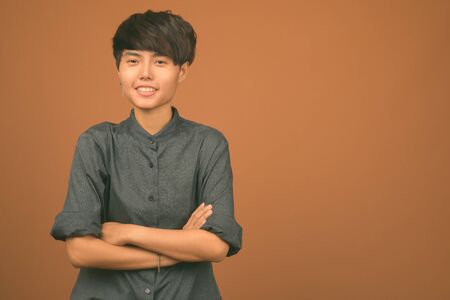 Young beautiful Asian woman with short hair against brown backgroundの写真素材