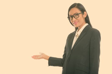 Studio shot of young happy Asian businesswoman smiling while showing somethingの写真素材