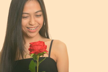 Young happy Asian teenage girl smiling while holding red roseの写真素材