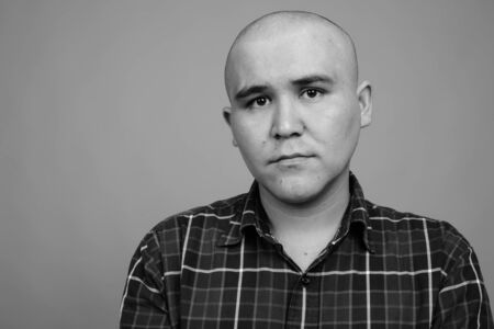 Young bald Asian businessman against gray backgroundの写真素材
