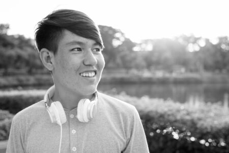 Young Asian teenage boy wearing headphones while relaxing at the parkの写真素材