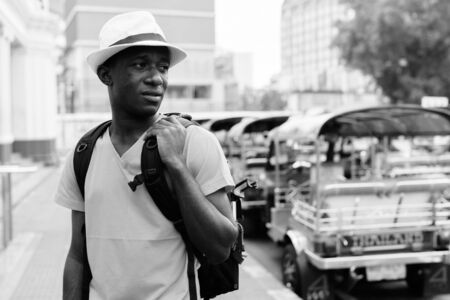 Young African tourist man thinking while holding backpack and sightseeing at railway stationの写真素材