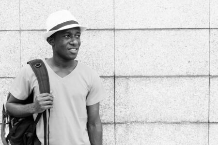 Young African tourist man holding backpack while thinking against concrete block wallの写真素材
