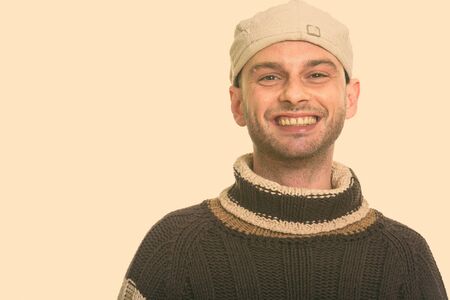 Studio shot of young happy man smiling while wearing hat