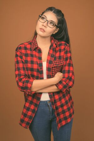 Young beautiful Asian woman wearing red checkered shirt against brown backgroundの写真素材