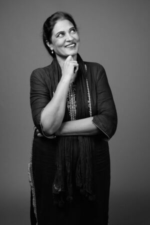 Happy mature beautiful Indian woman against gray backgroundの写真素材